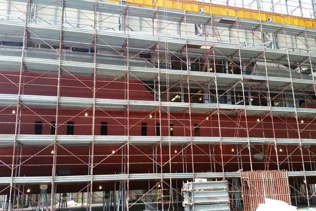 Impalcature attorno a un edificio rosso in costruzione, con operai visibili ai piani superiori.