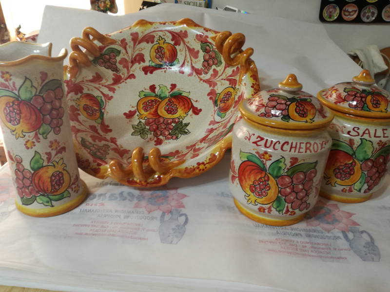 Set di utensili da cucina in ceramica con motivo di frutta: vaso, ciotola e due barattoli con coperchio nei colori giallo, arancione e rosso.