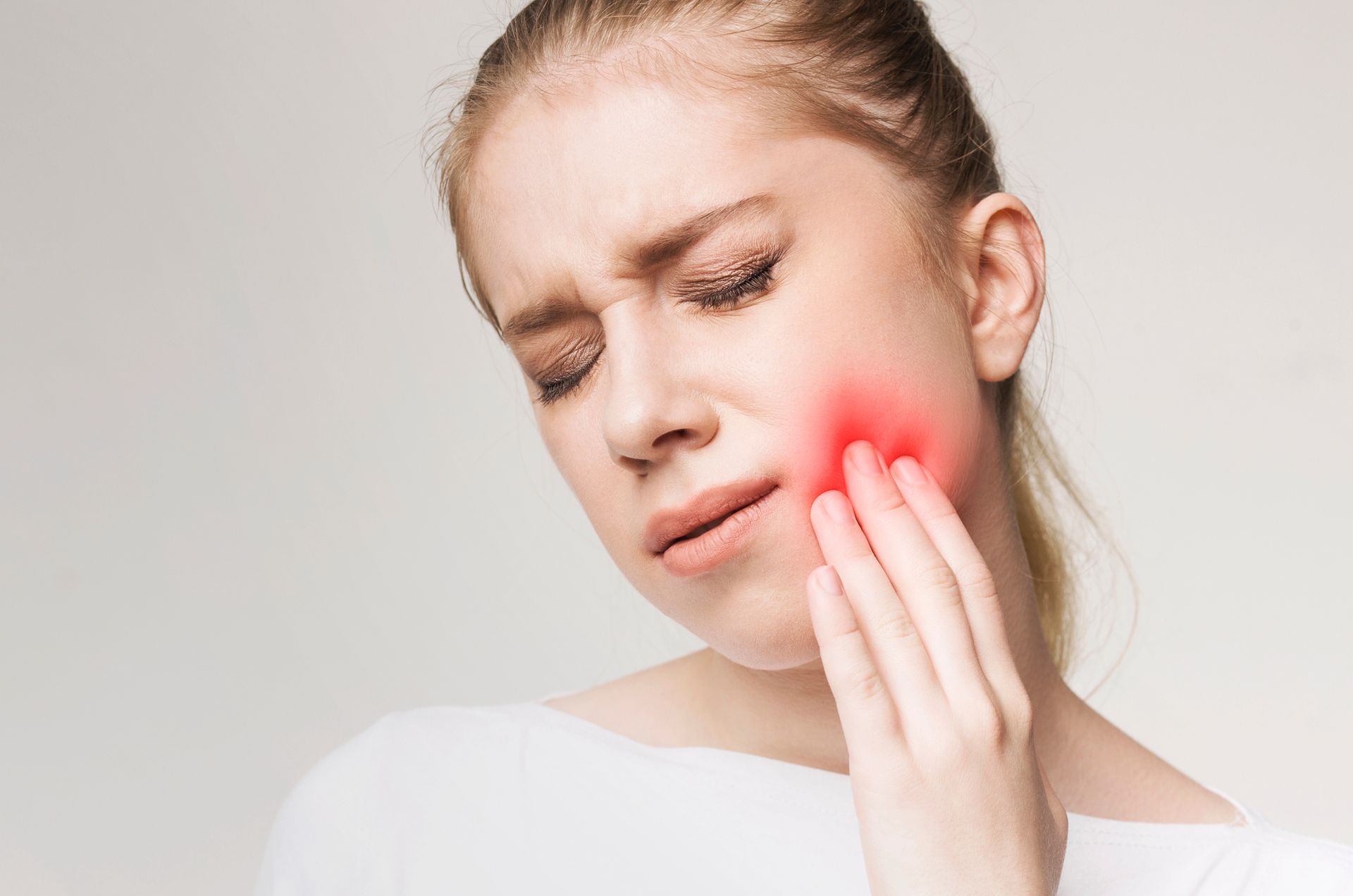 Una persona si tiene la guancia, evidenziando un'area rossa e luminosa, indice di mal di denti o dolore al viso, su uno sfondo chiaro.