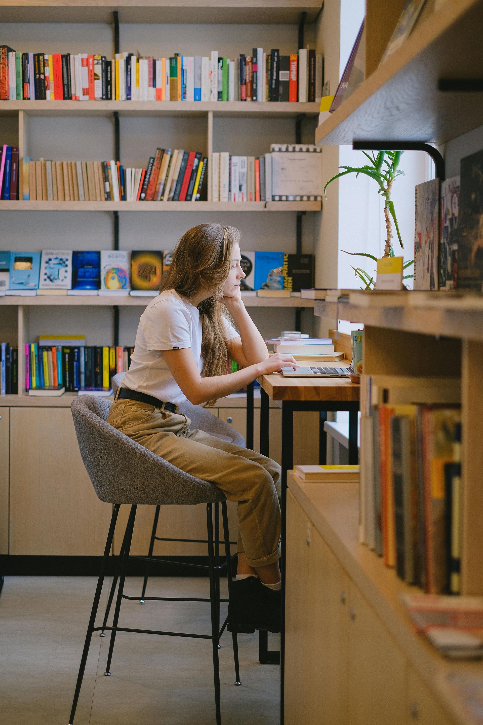 Woman on phone in bright office, working at a desk with a laptop and papers while colleagues meet in background
