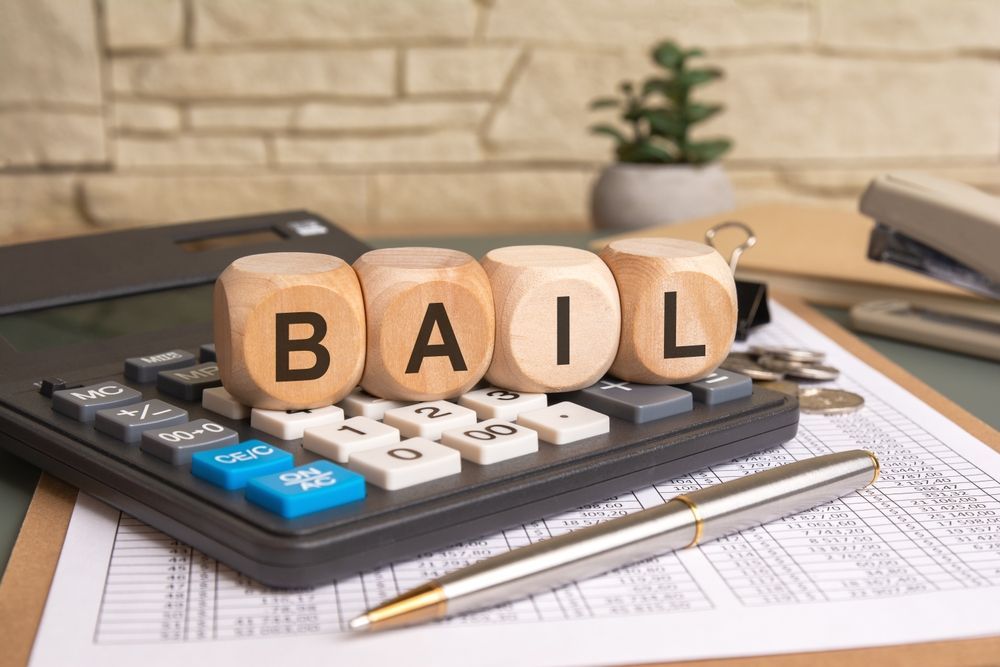 Calculator with wooden blocks spelling “BAIL” on paperwork, with a pen and laptop nearby.