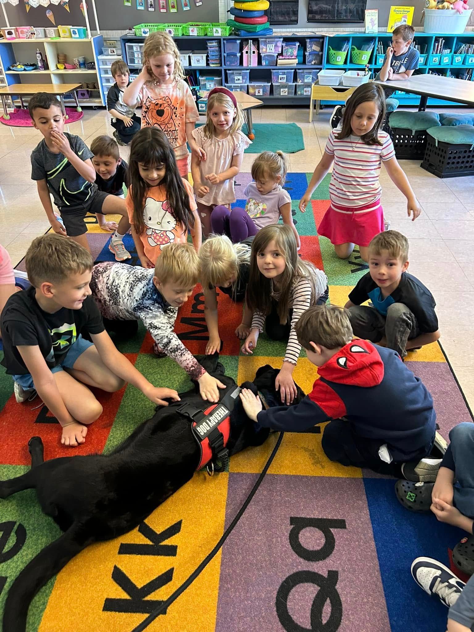 Children sitting on a colorful classroom rug, gathered around a large black-and-red robot toy.