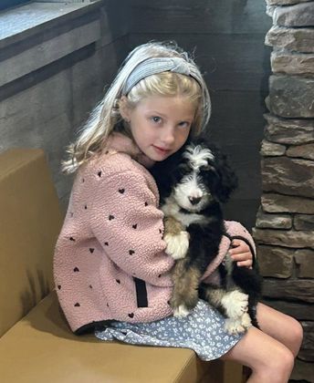 Girl in a pink sweater holding a black-and-white puppy on a stair landing