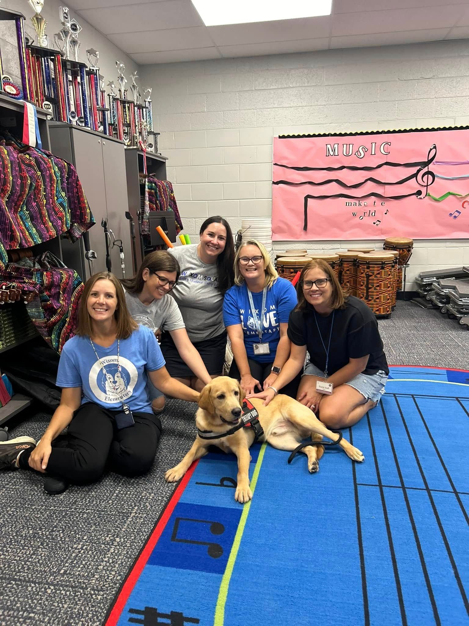 Group posing with two dogs in a colorful room with hanging ribbons and a pink banner