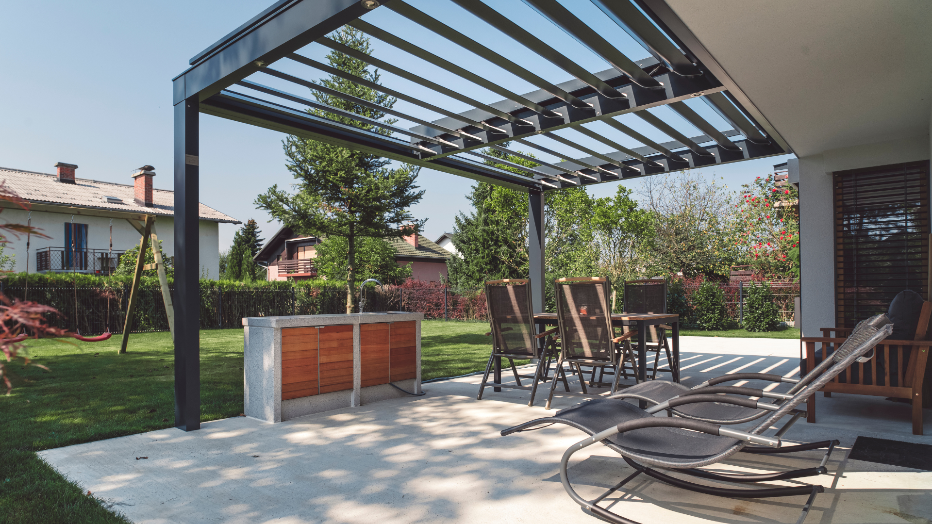 A patio with a pergola , chairs , a table and a sink.
