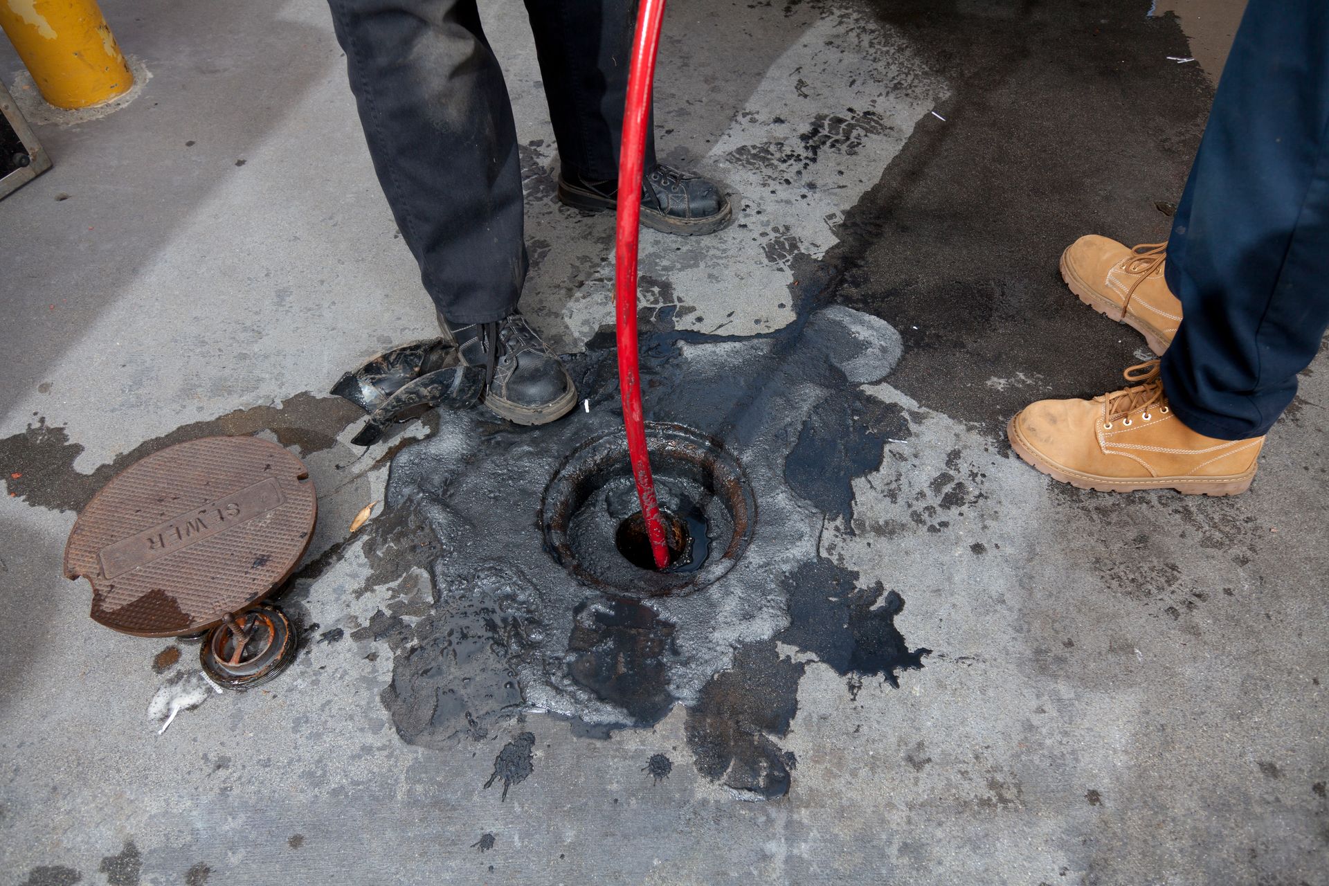 A man is kneeling down in front of a manhole cover.