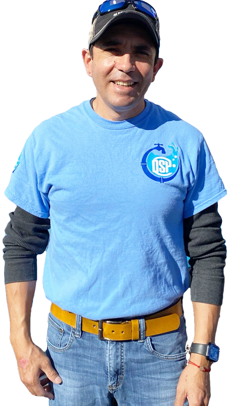 A man in overalls is holding a wrench and smiling.