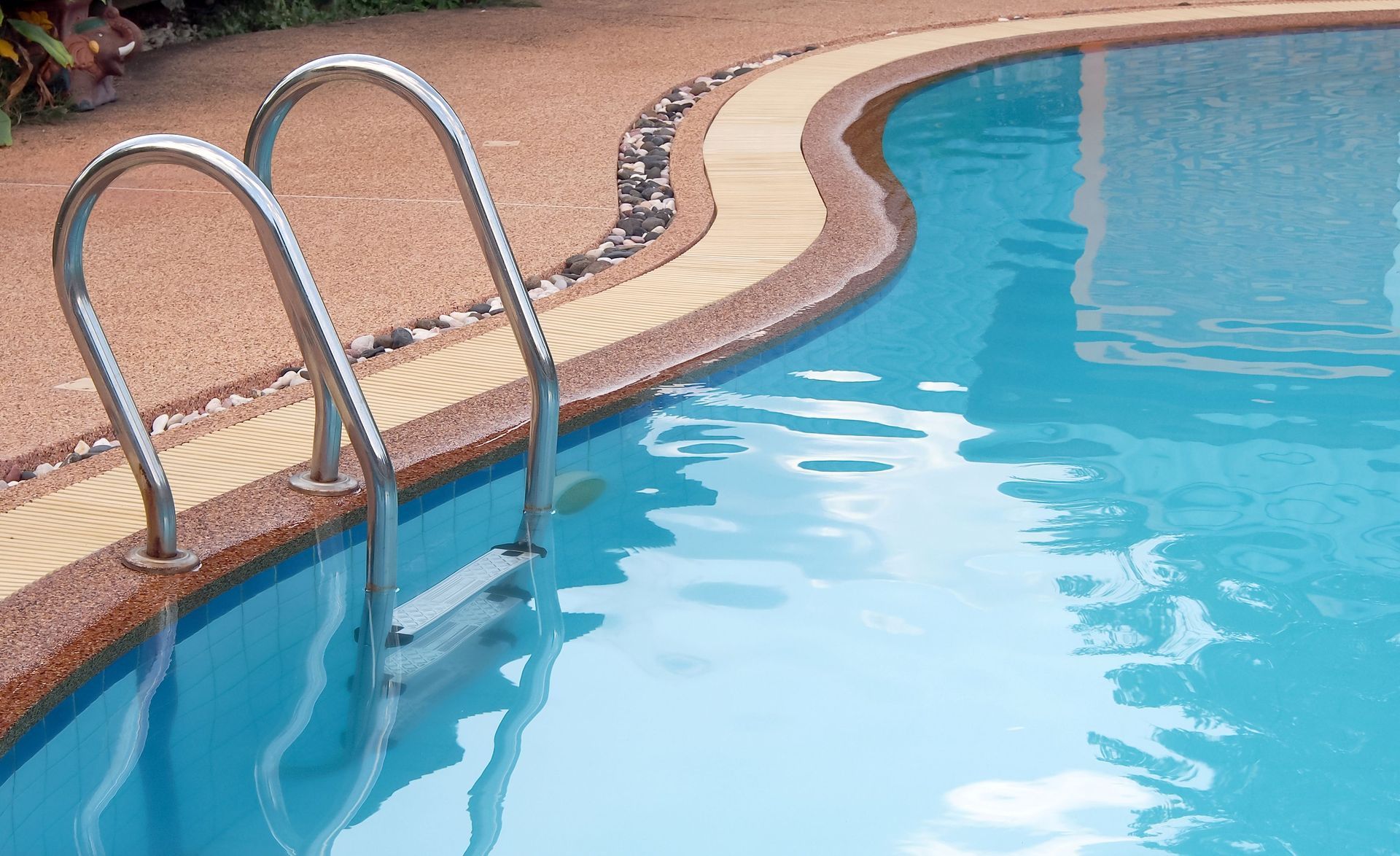 Swimming pool ladder beside a blue pool with brick decking and tiled edge