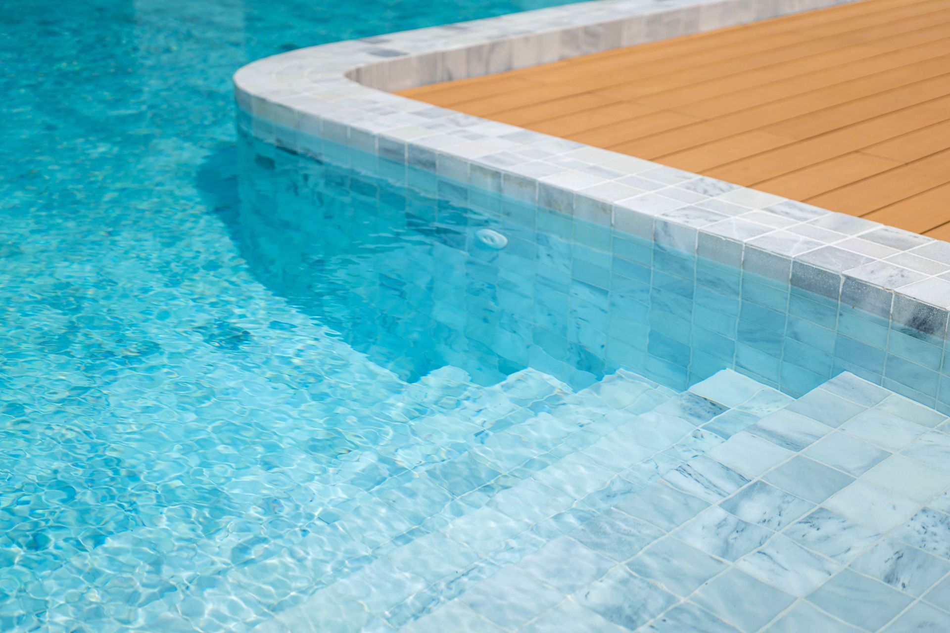 Blue pool water beside a curved white edge and light wood deck