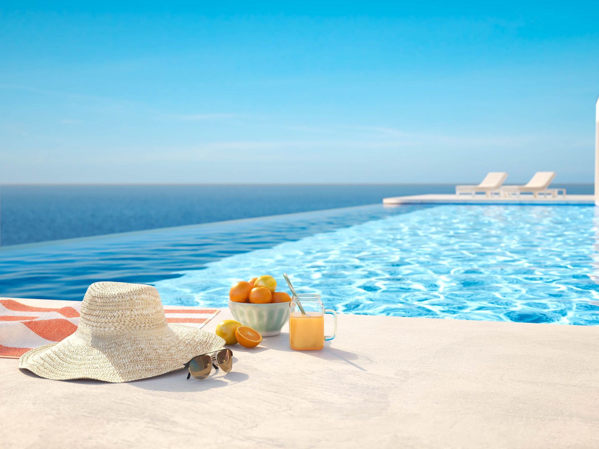 Sunny poolside deck with hat, sandals, drinks, and an infinity pool overlooking the ocean