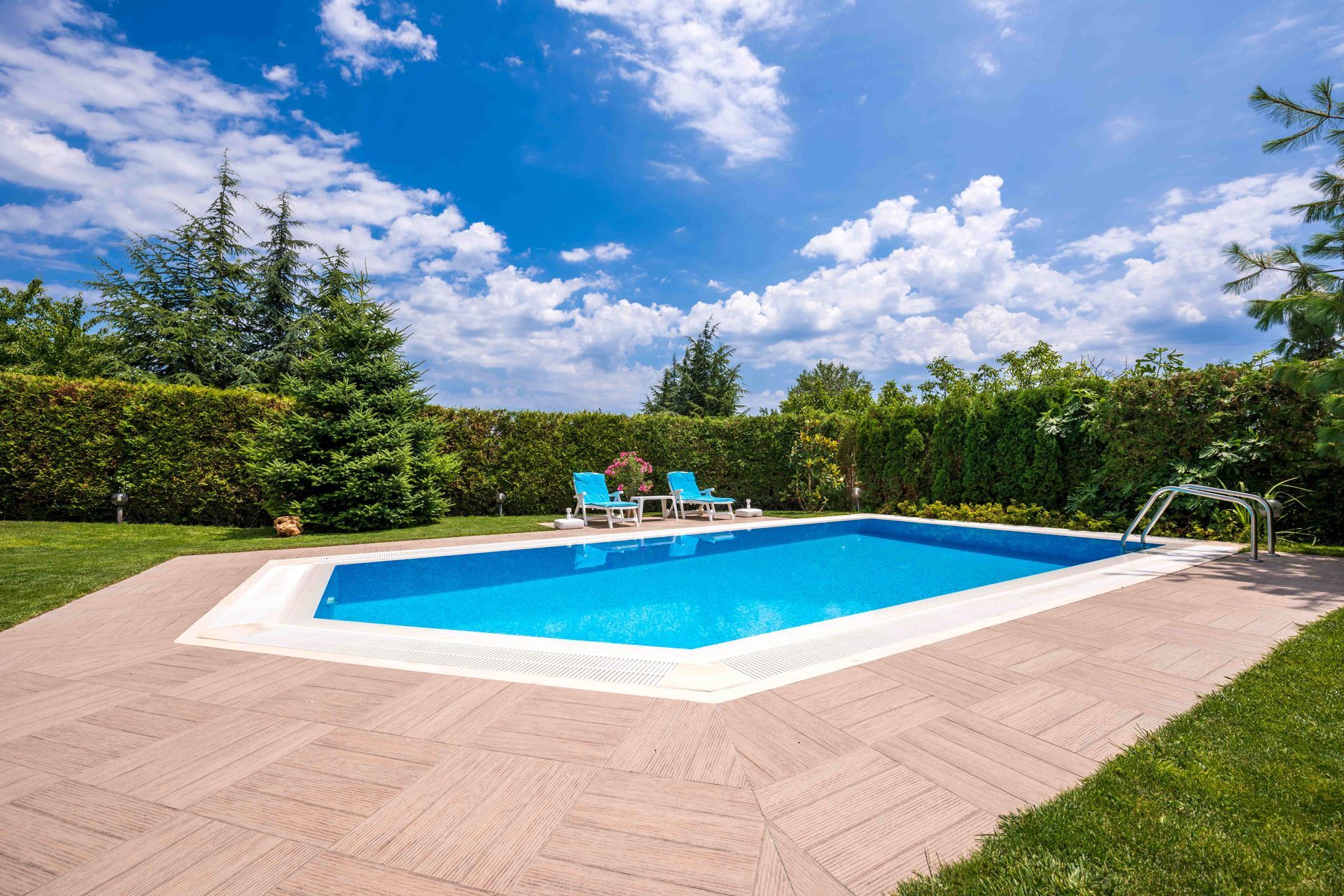 Backyard pool with blue water, lounge chairs, and trees under a bright sky