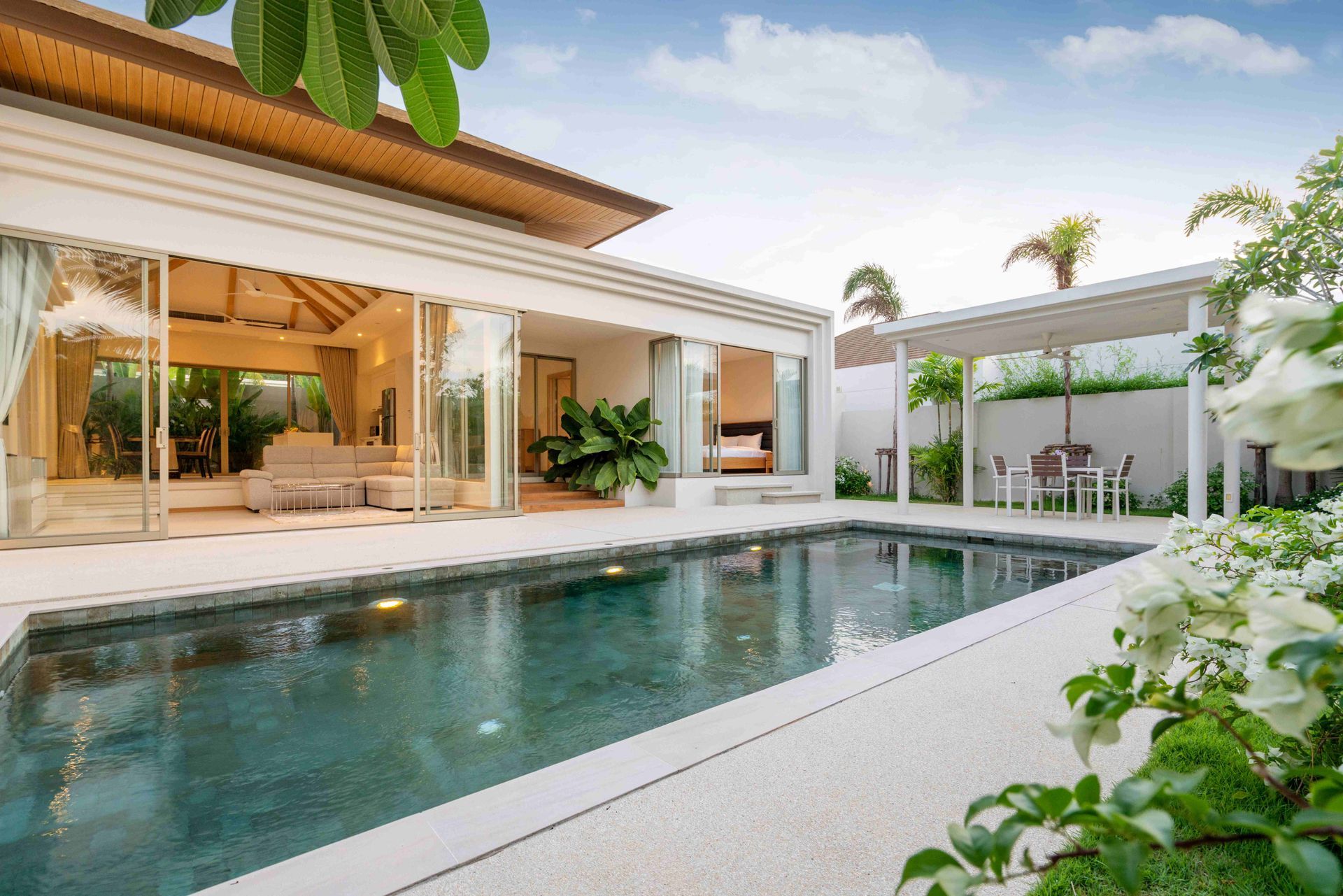 Modern patio with a long reflecting pool, open indoor-outdoor seating, and lush tropical greenery