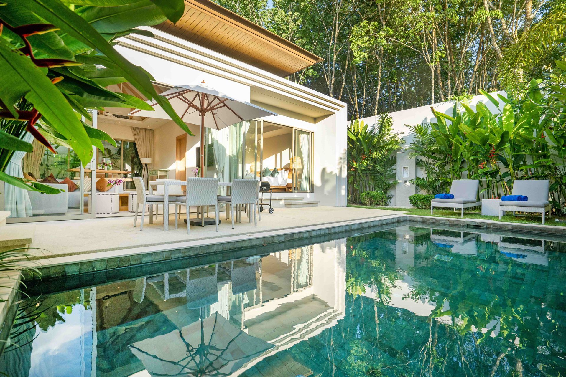 Modern house patio with a dining area beside a clear blue swimming pool and lush greenery Modern house patio with a dining area beside a clear blue swimming pool and lush greenery