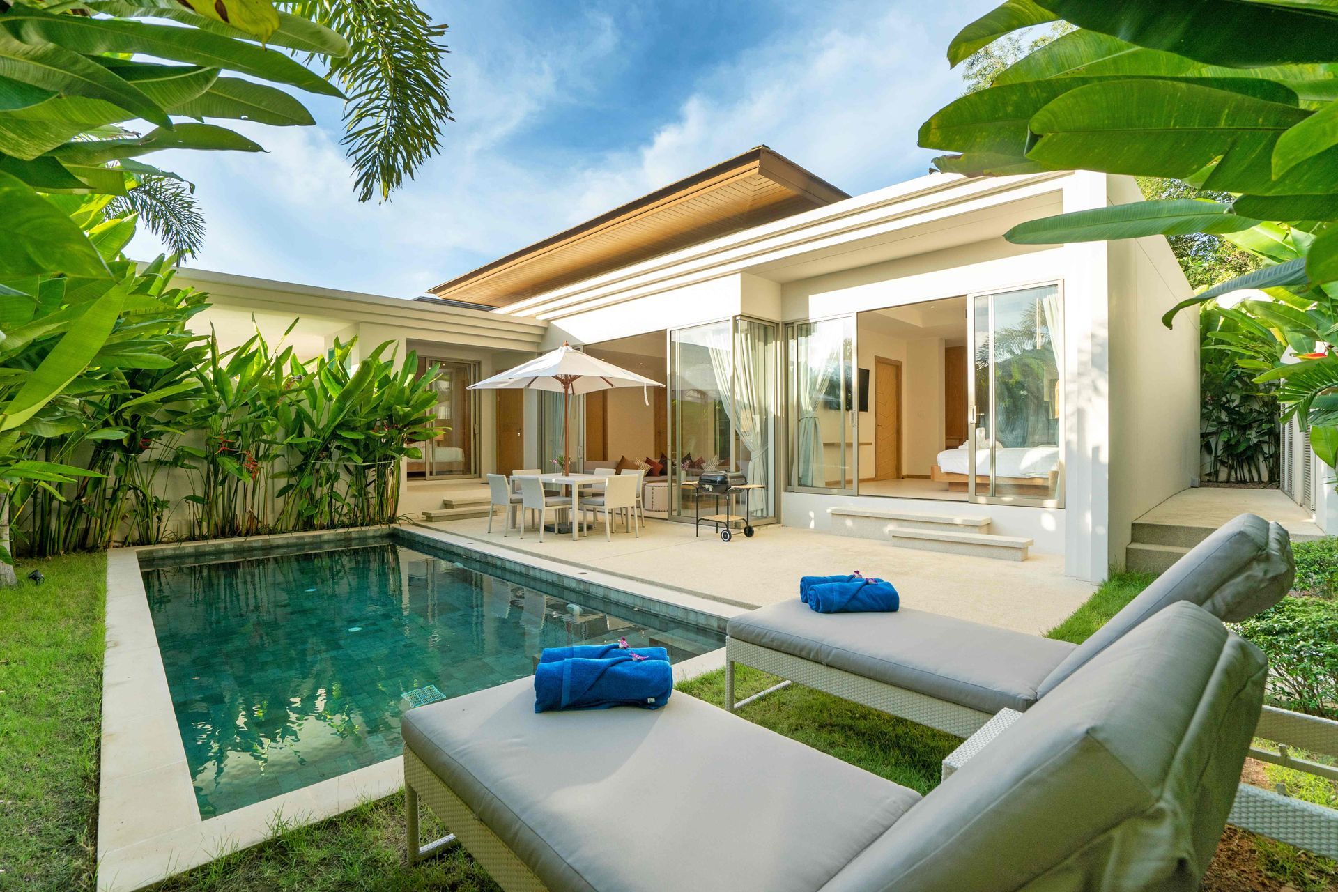 Modern villa patio with a small pool, lounge chairs, and open glass doors surrounded by lush greenery