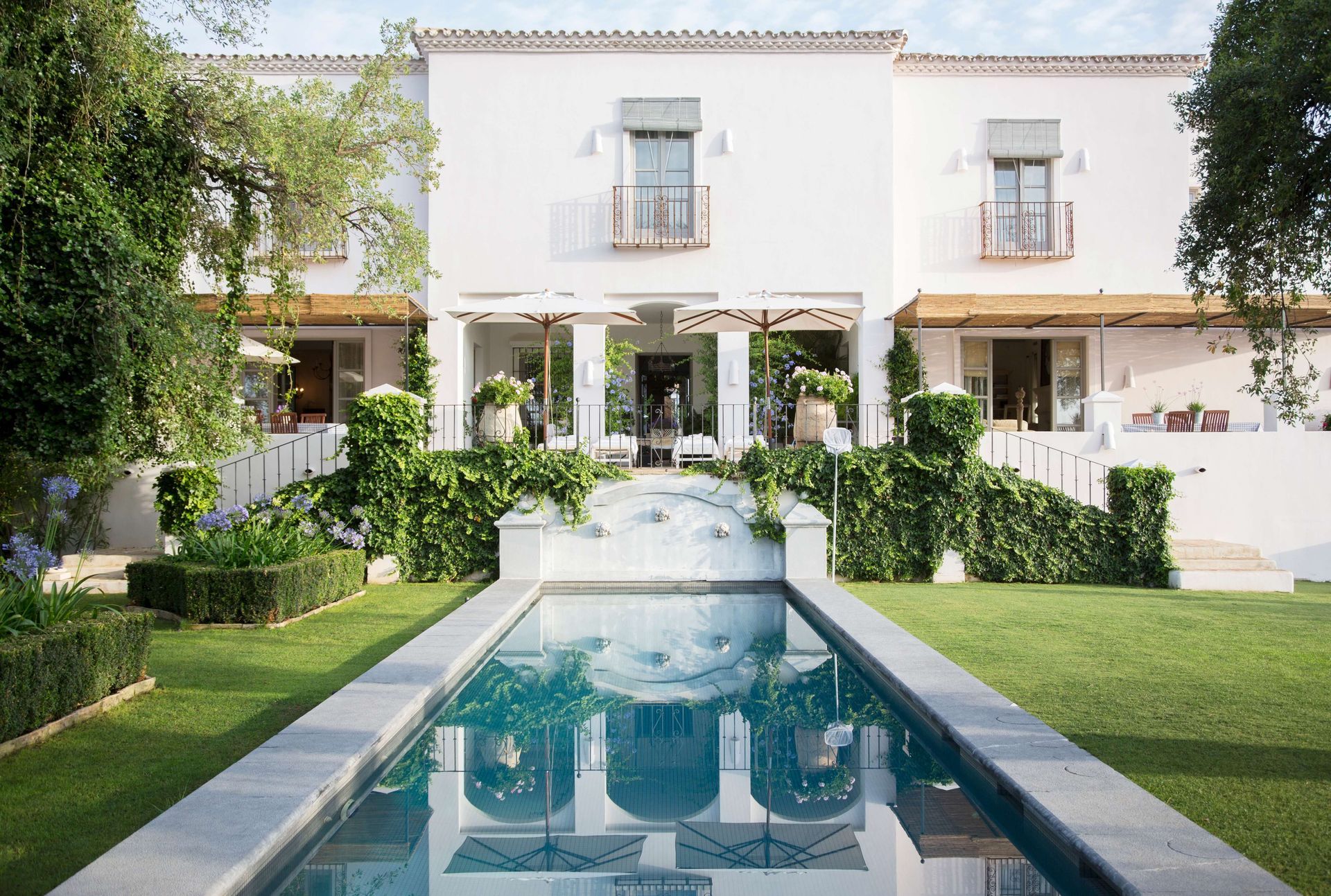 Modern white villa with a long turquoise pool and manicured greenery in front