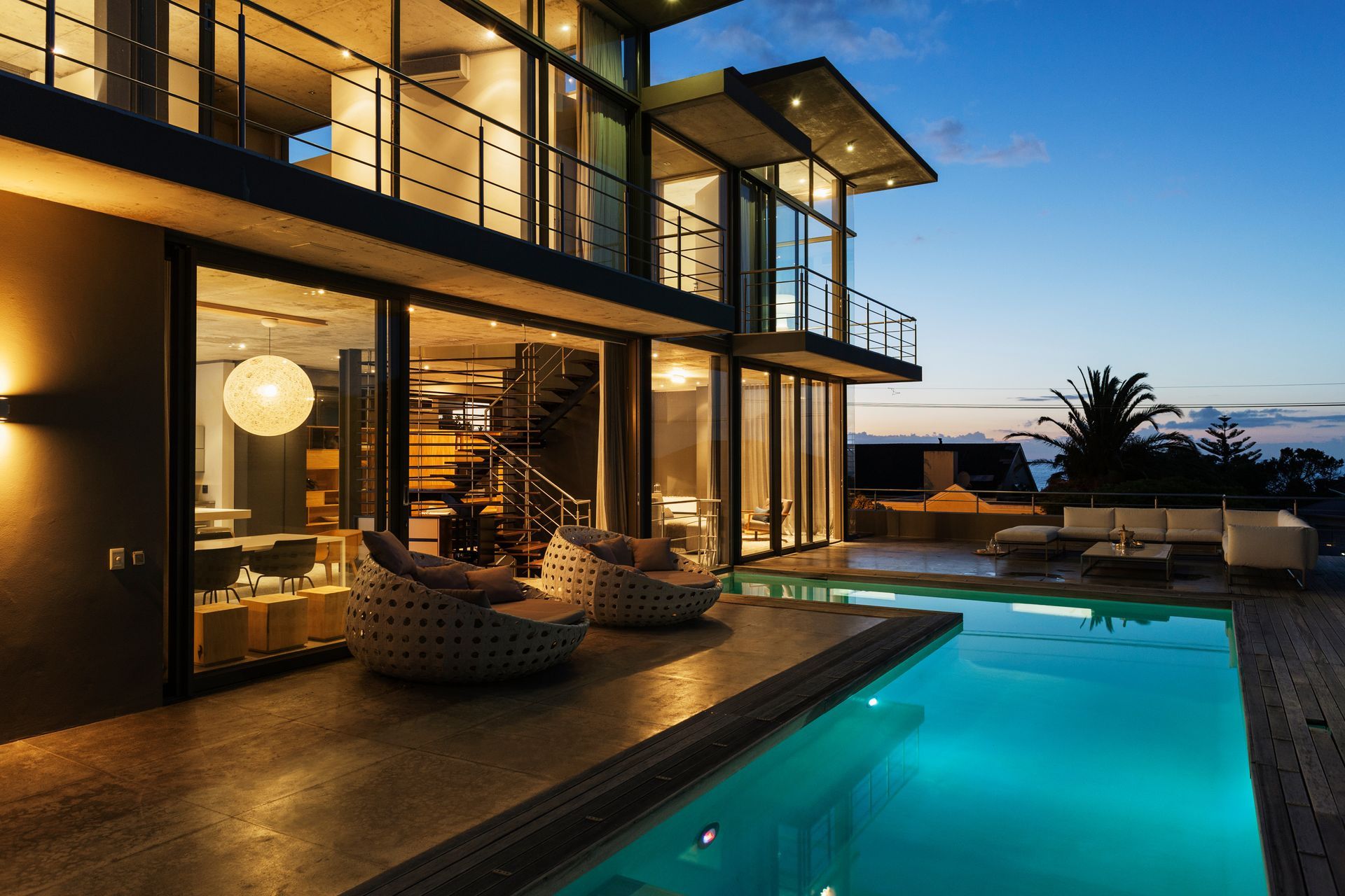 Modern luxury house with lit patio and turquoise pool at dusk