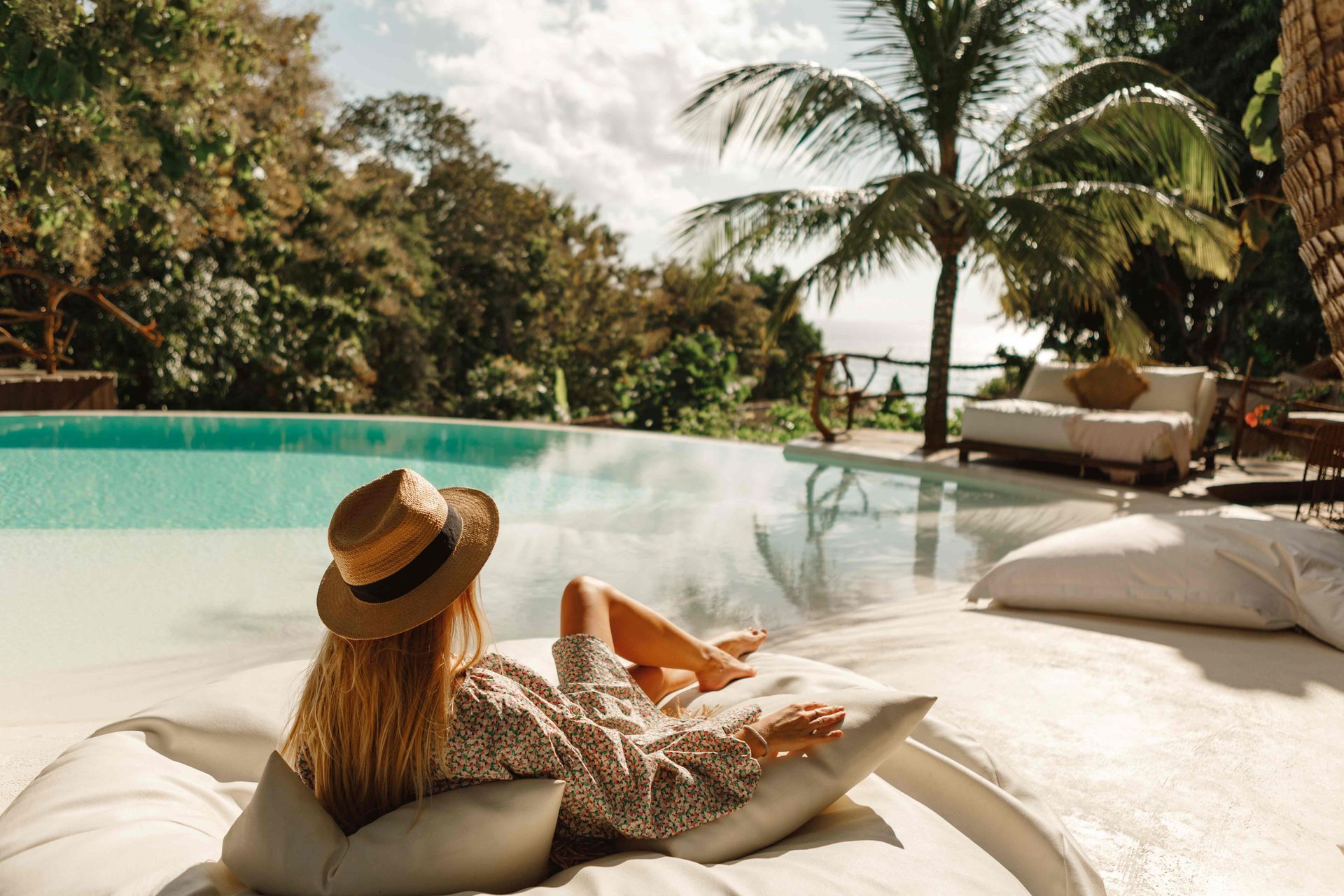 Woman lounging by a turquoise infinity pool with tropical trees and a sunny resort view