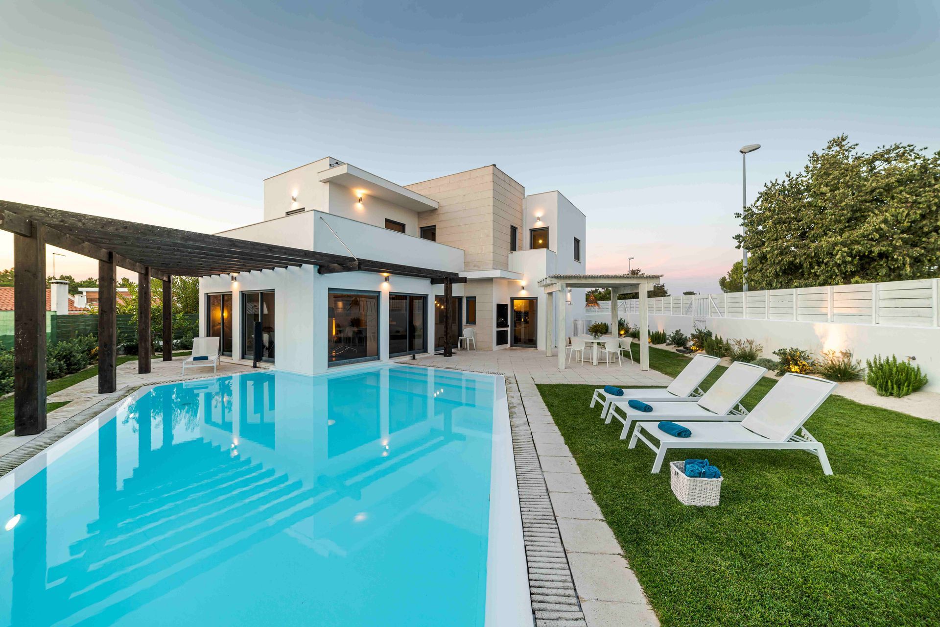 Modern house with a turquoise swimming pool, lounge chairs, and a green lawn at sunset