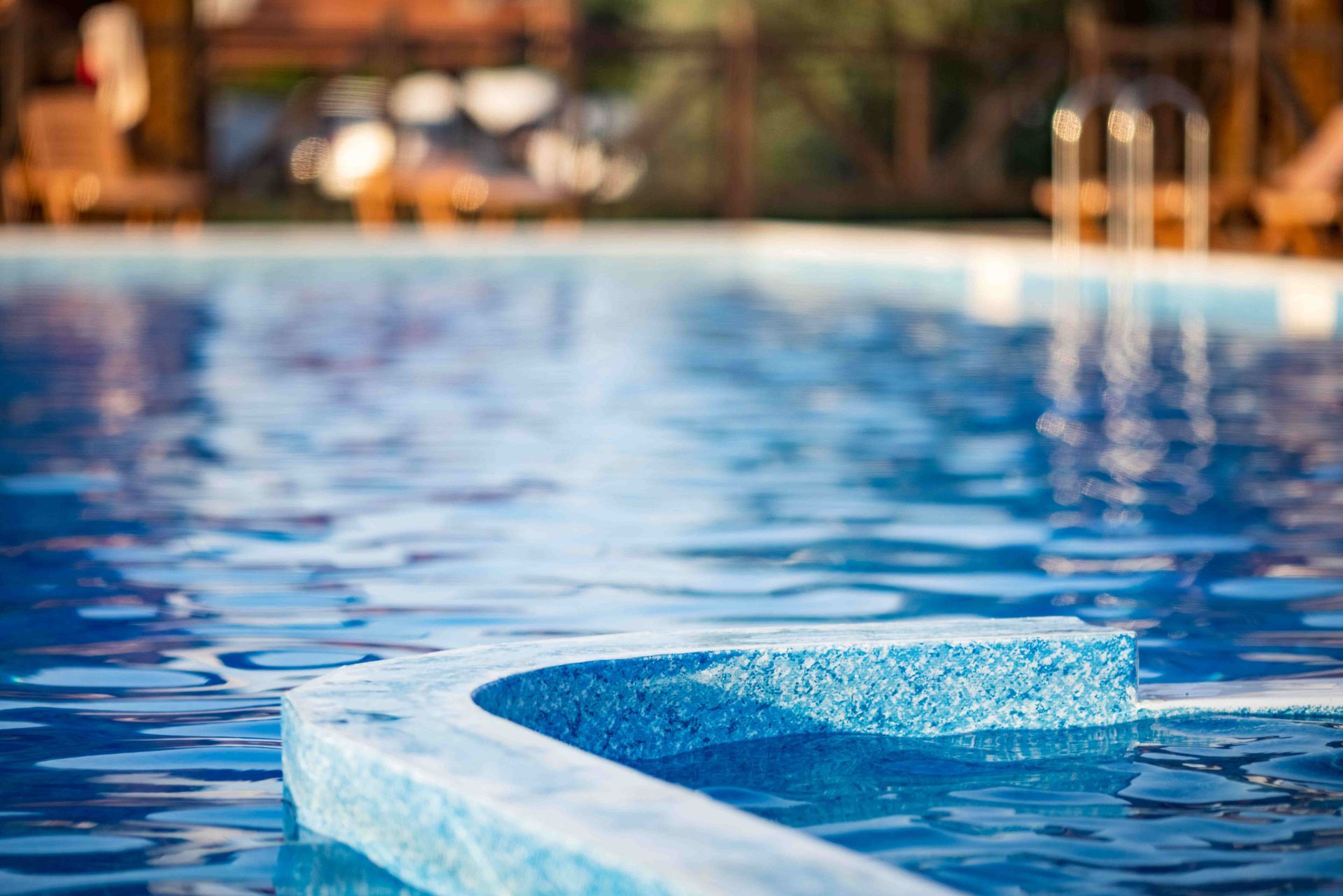 Outdoor swimming pool with clear blue water and a white edge, blurred lounge area in the background