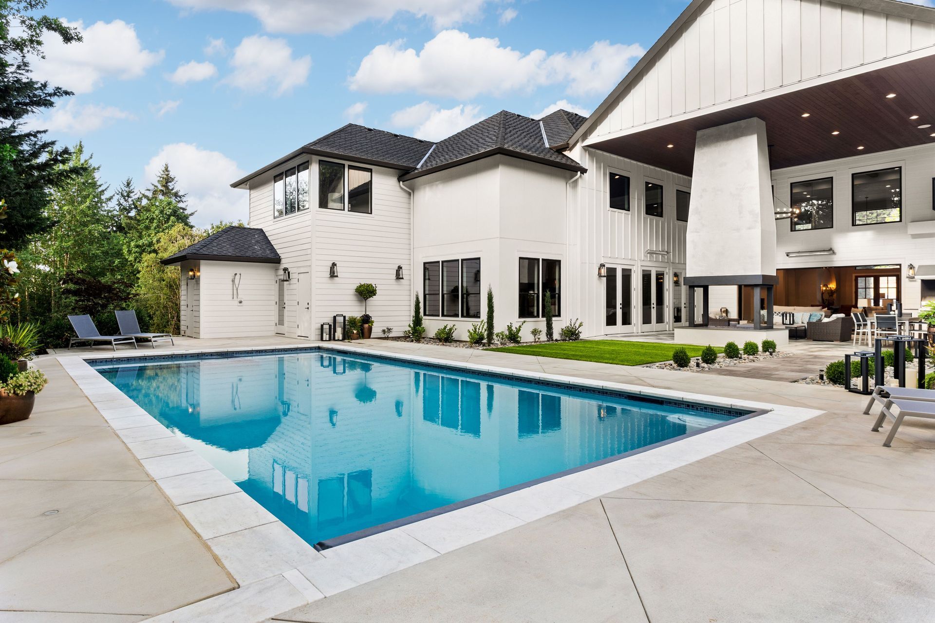 Modern white house with a backyard swimming pool and patio under a bright sky