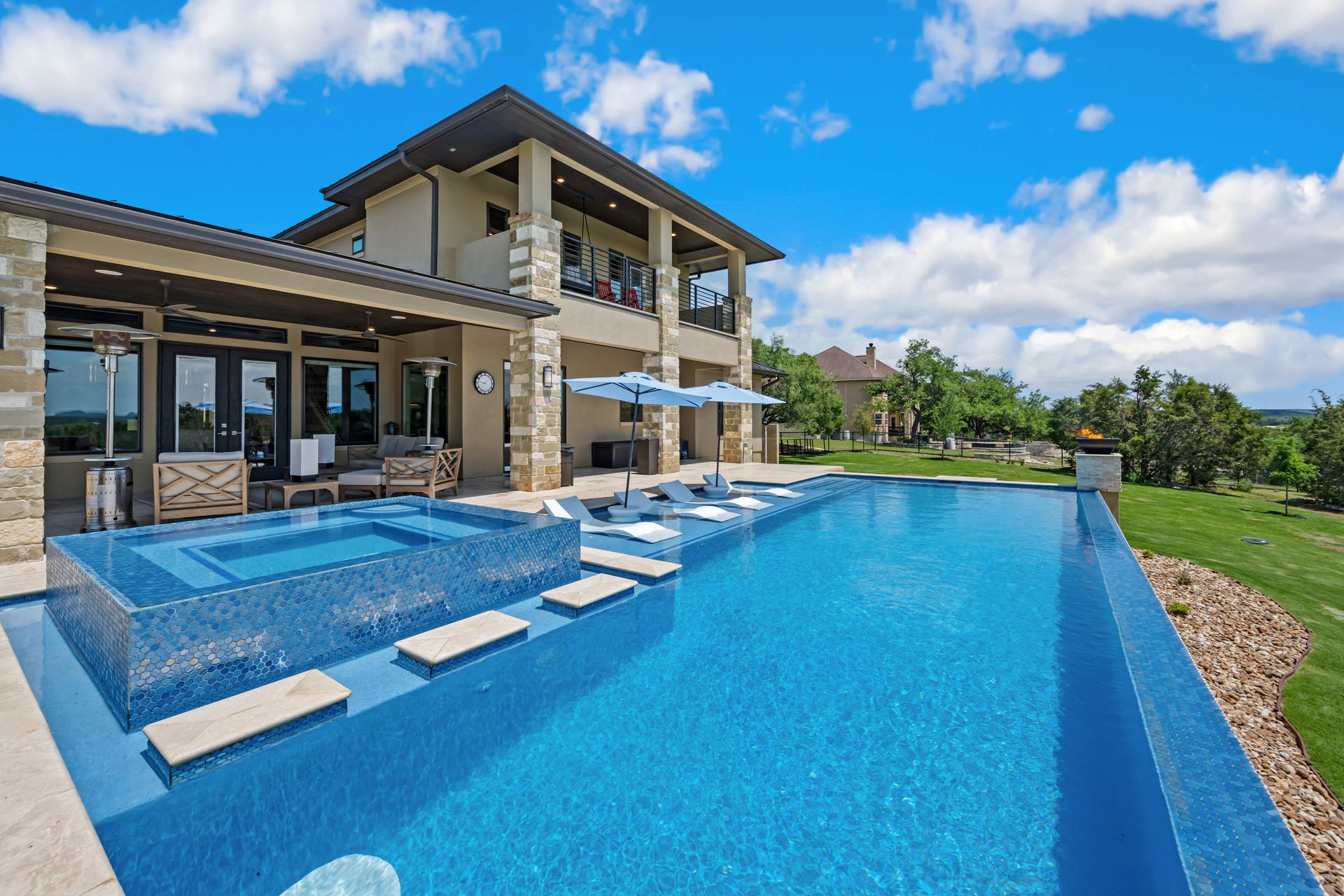 Modern luxury villa with a large blue infinity pool and stone patio under a bright sky