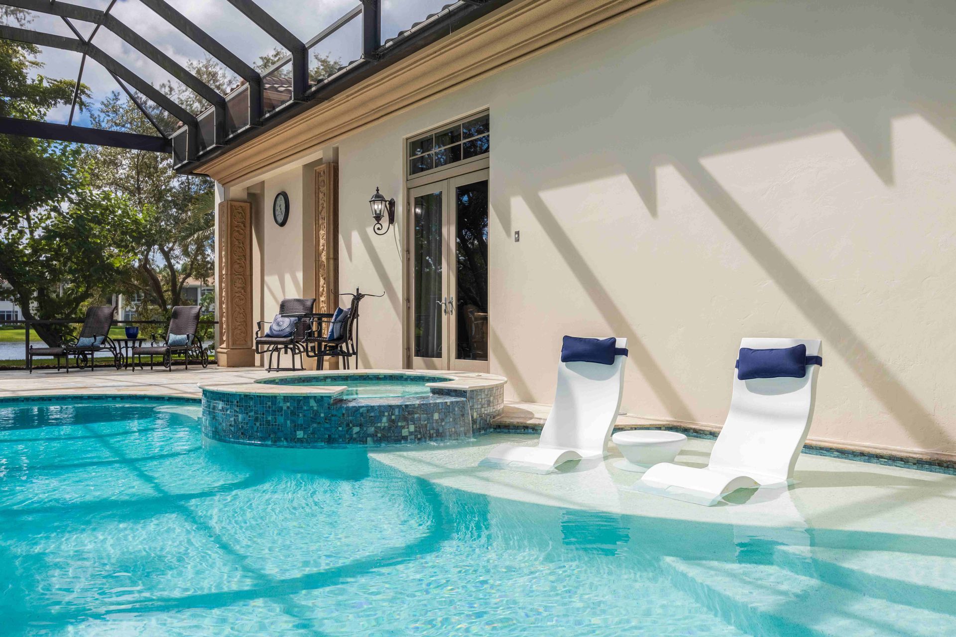 Backyard pool with two white lounge chairs under a covered patio and glass enclosure