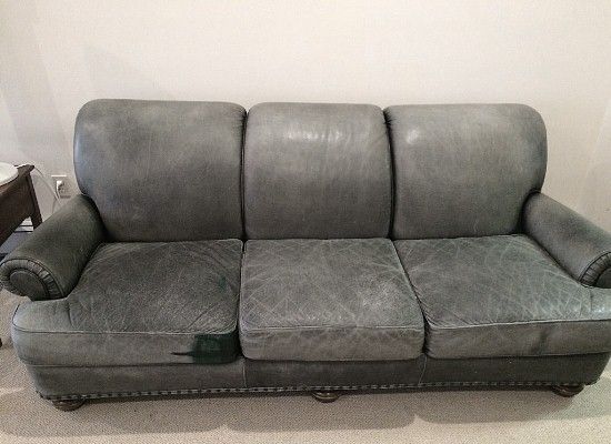 Blue leather three-seat sofa with wear and tear, in a room.