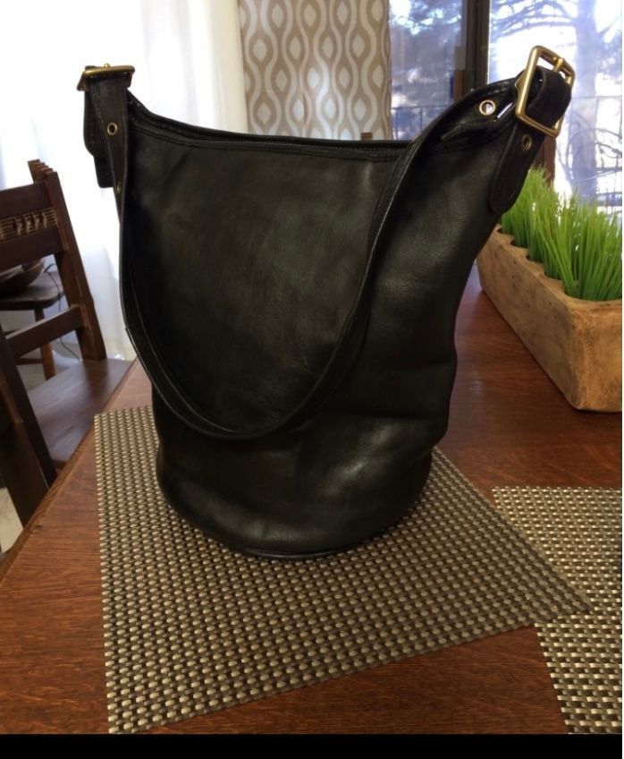 Black leather Coach shoulder bag with brass buckles on a table.