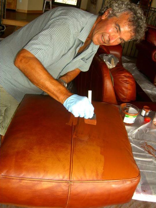 Man in blue gloves restoring brown leather cushion with brush.