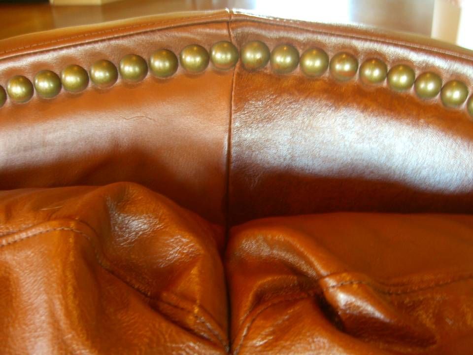 Close-up of brown leather upholstery with brass-colored nailhead trim.
