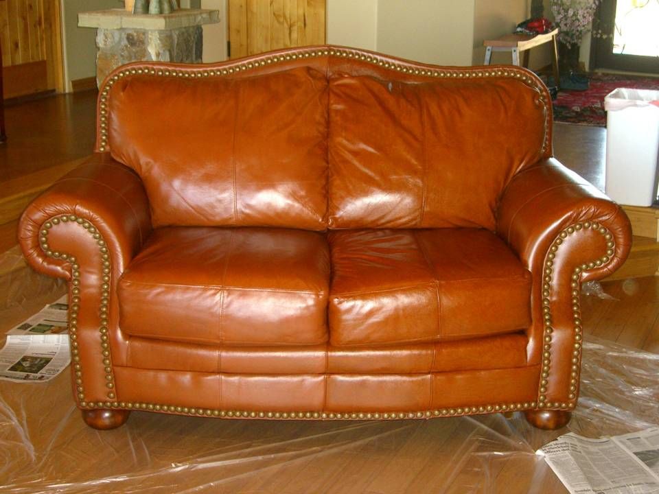Brown leather loveseat with nailhead trim on protective plastic in a living room.