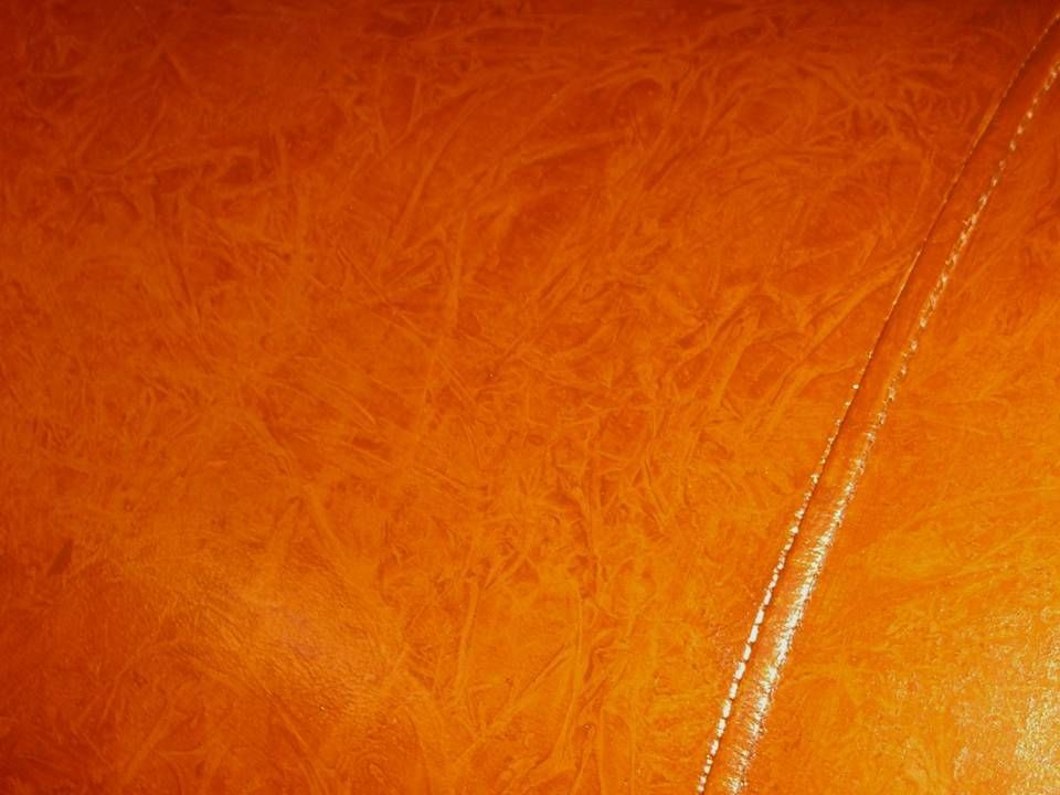 Close-up of orange leather with a visible stitch.
