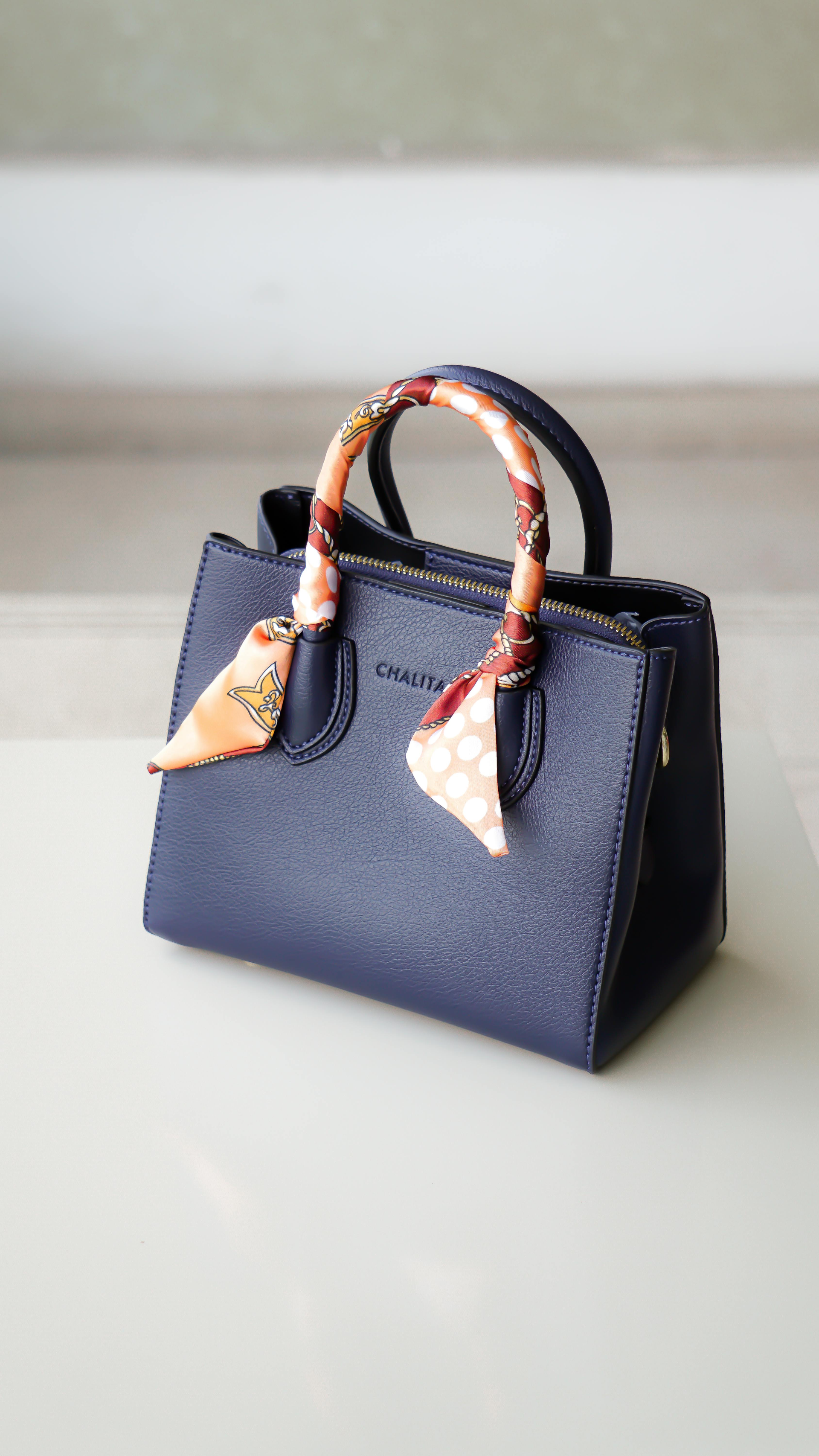Navy blue handbag with a patterned scarf tied around the handles.