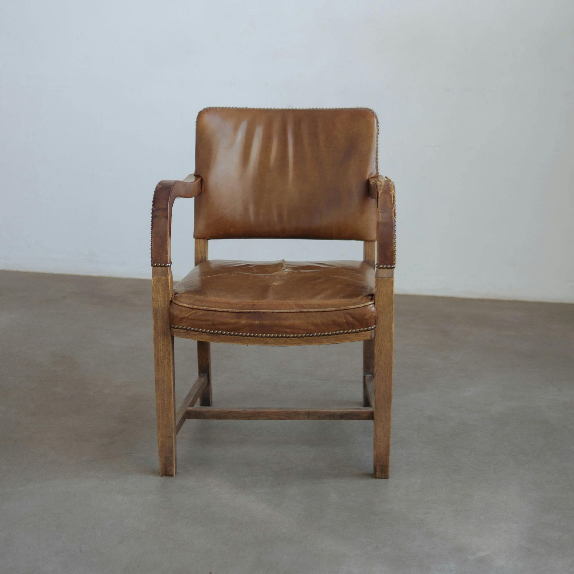 Wooden chair with tan leather seat and back, set against a neutral wall and floor.
