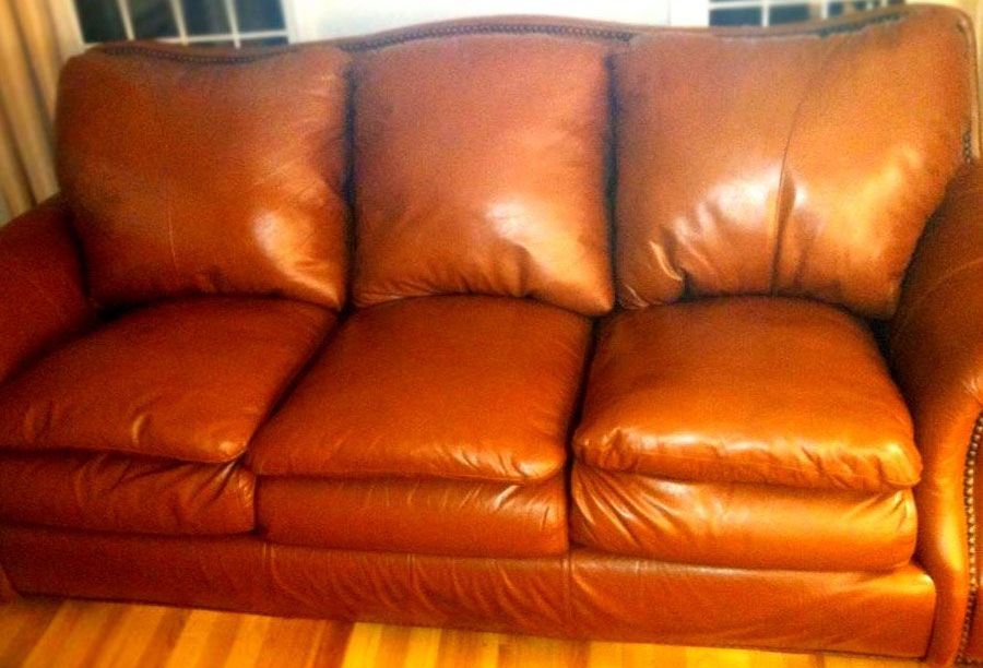 Brown leather three-cushion sofa in a room with a wood floor, lit by natural light.