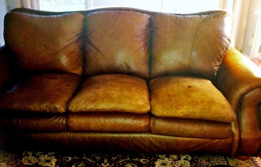 Brown leather sofa with three cushions in front of a window.