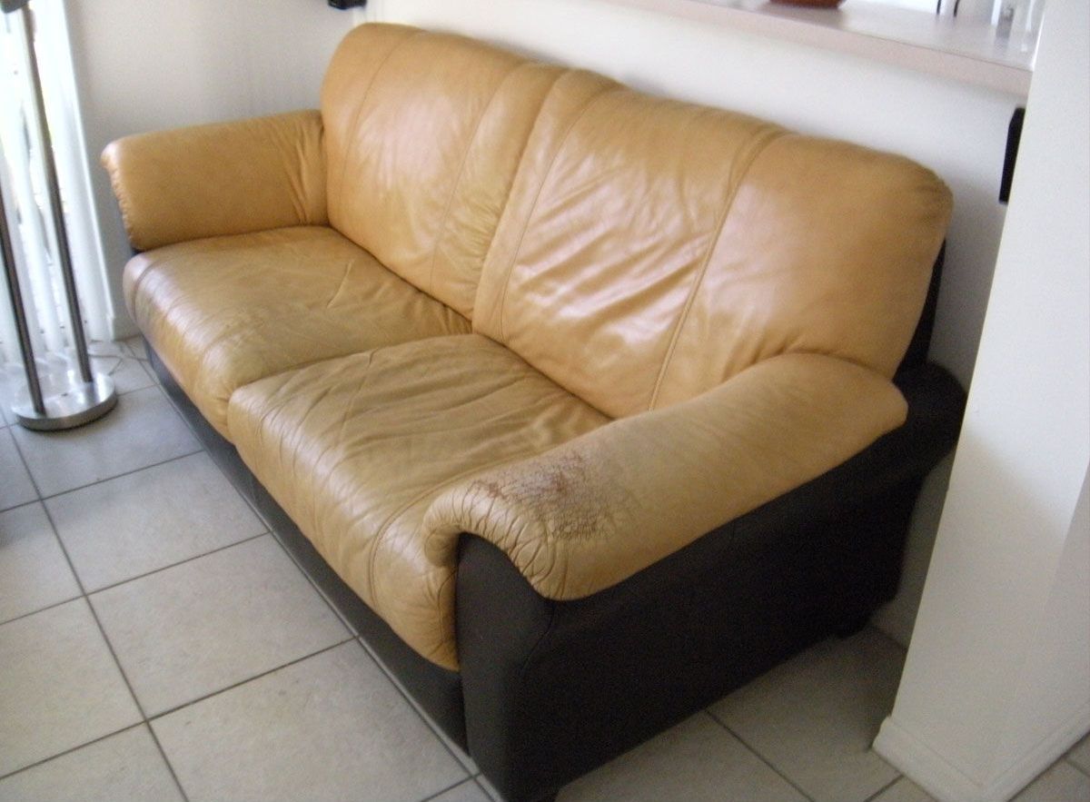 Yellow leather couch with dark brown base in a room with white tile floor.