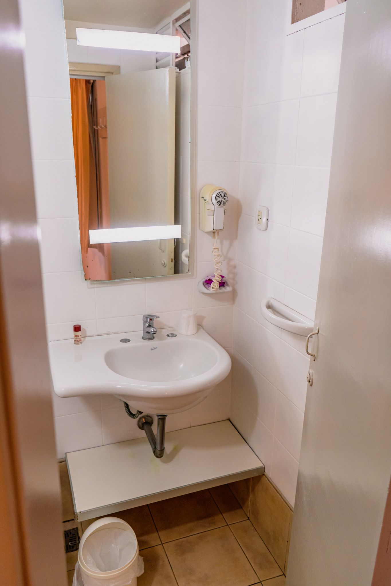 Small white bathroom with a sink, mirror, and a hair dryer on the wall.