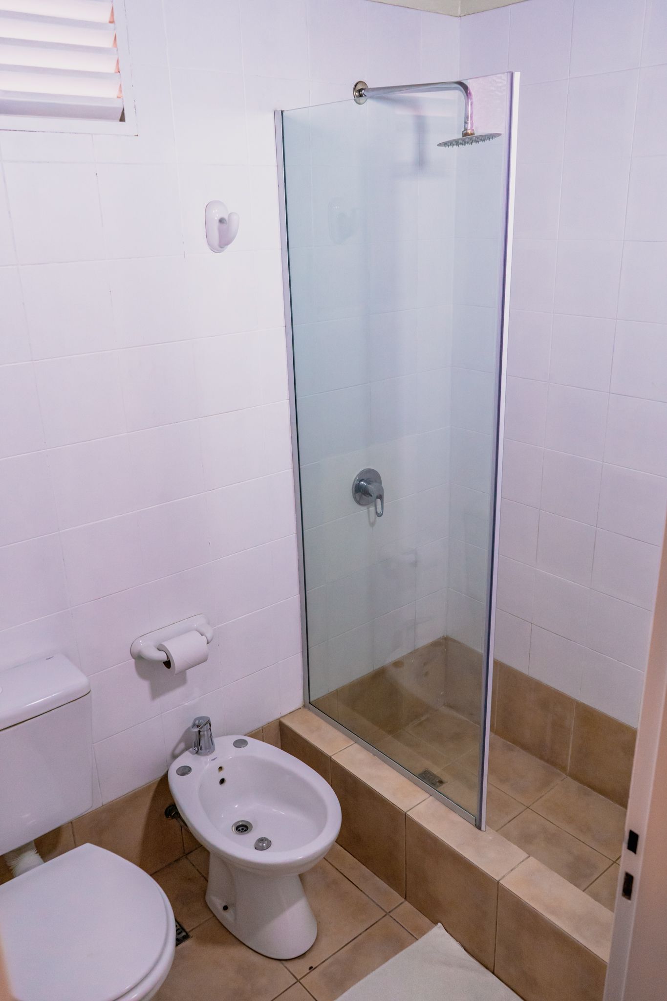 Bathroom with a toilet, bidet, and glass-doored shower. White walls, beige tile.