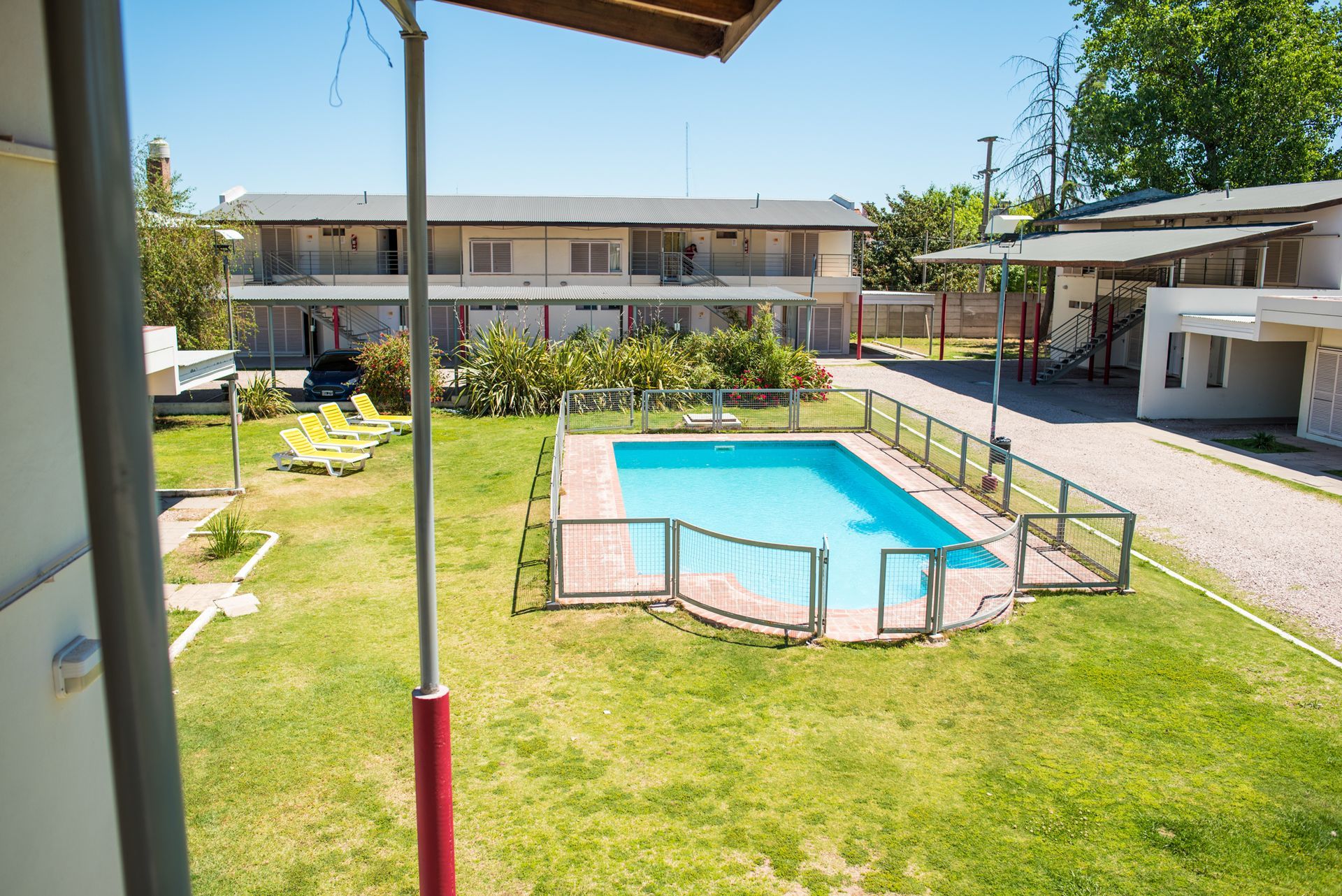Pool surrounded by a green lawn in front of a two-story building. Sunny day.