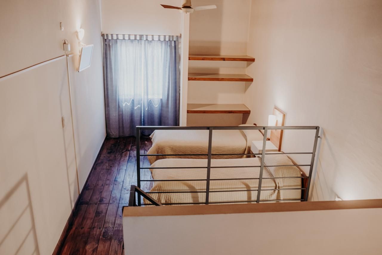 Loft bedroom with two beds, wooden floor, window with gray curtains, and built-in shelves.