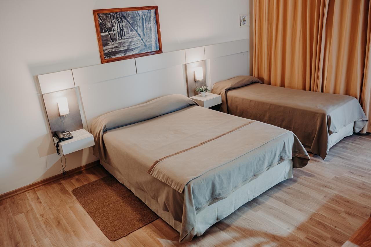 Two beds in a hotel room, one queen and one twin, with tan bedding, wood floors, and a framed painting.