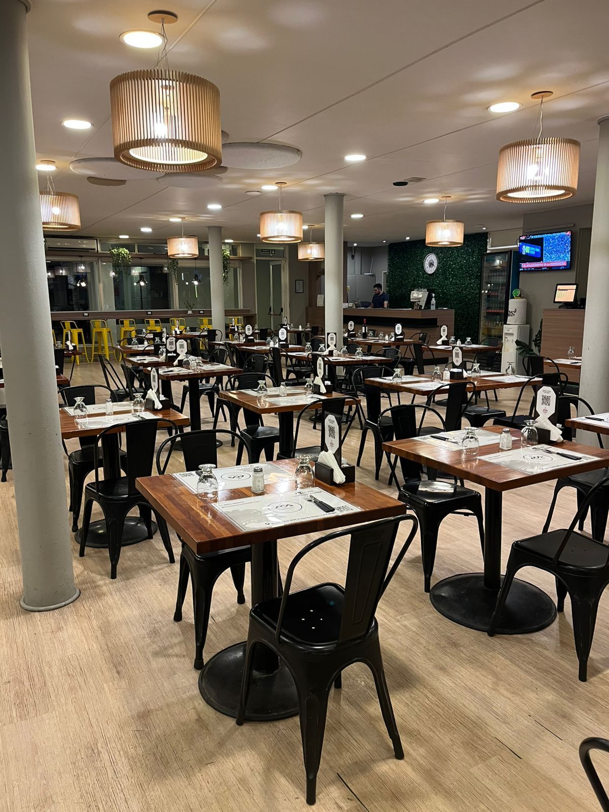 Restaurant interior: black chairs, square tables, pendant lights, and a green wall.
