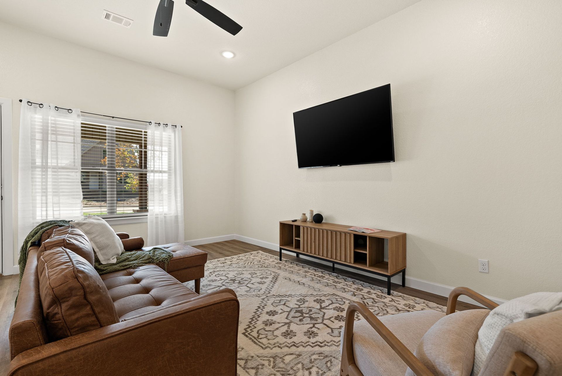 A living room with a couch , chair , television and ceiling fan.