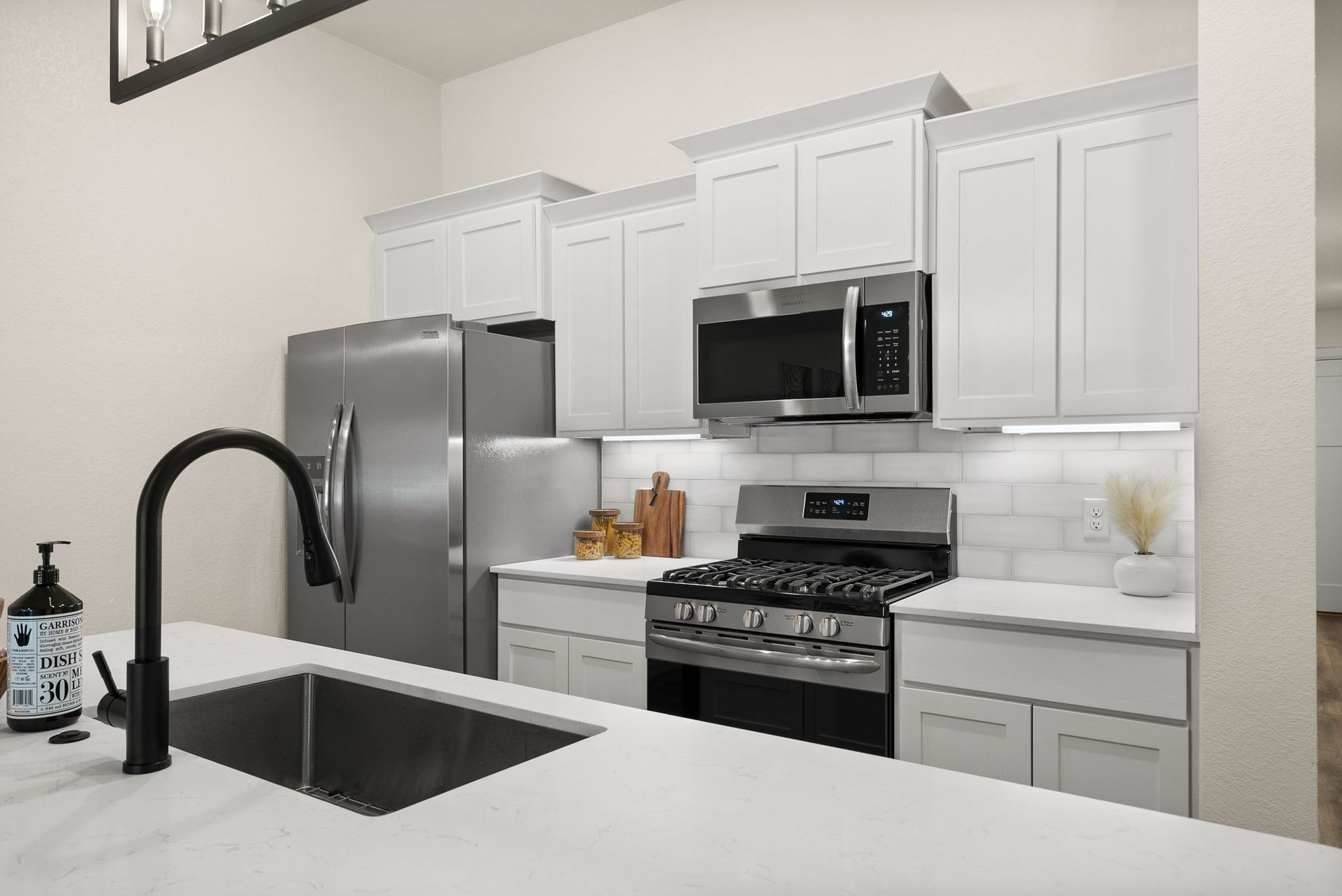 A kitchen with white cabinets , stainless steel appliances , a sink and a refrigerator.