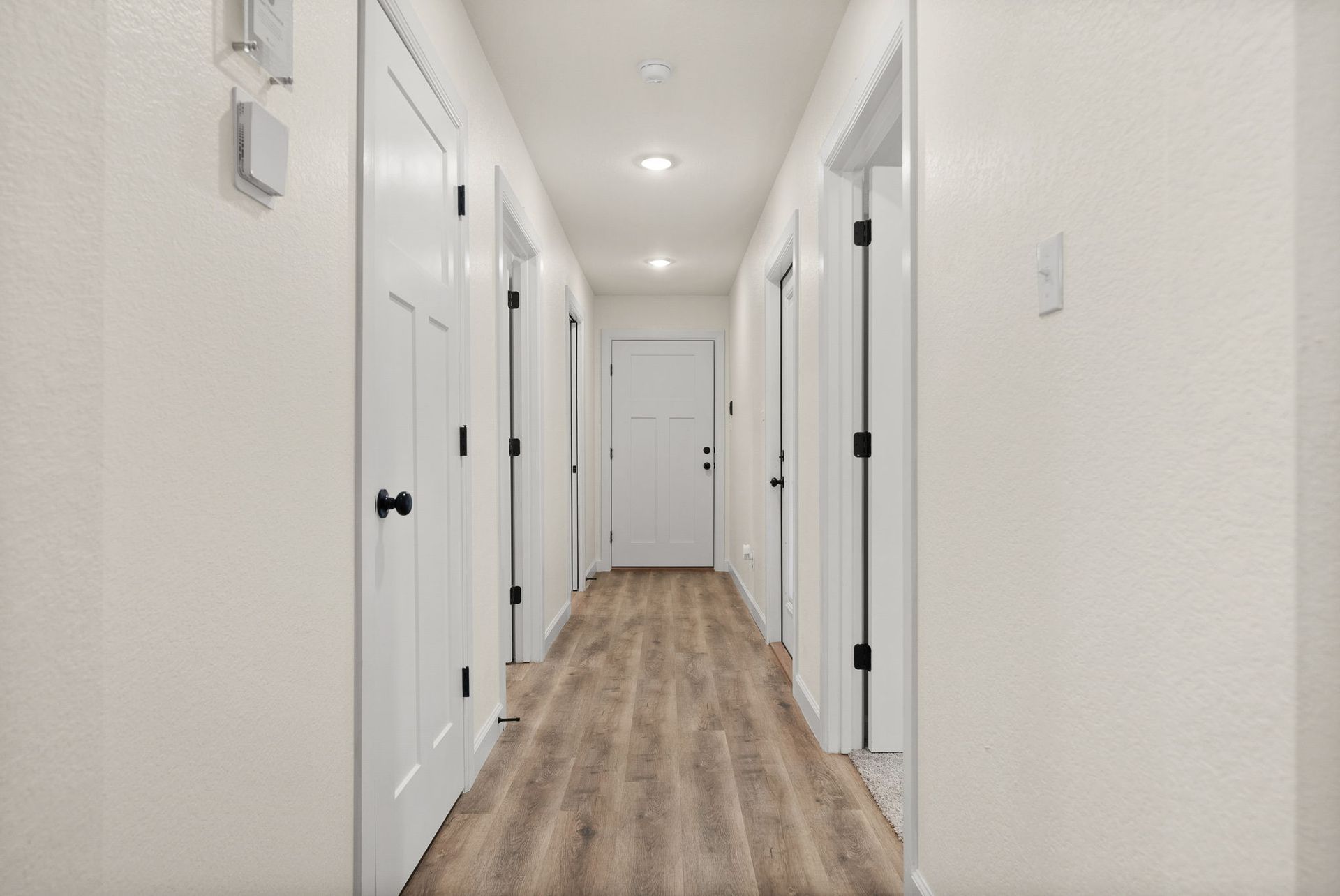 A long hallway with hardwood floors and white doors in a house.