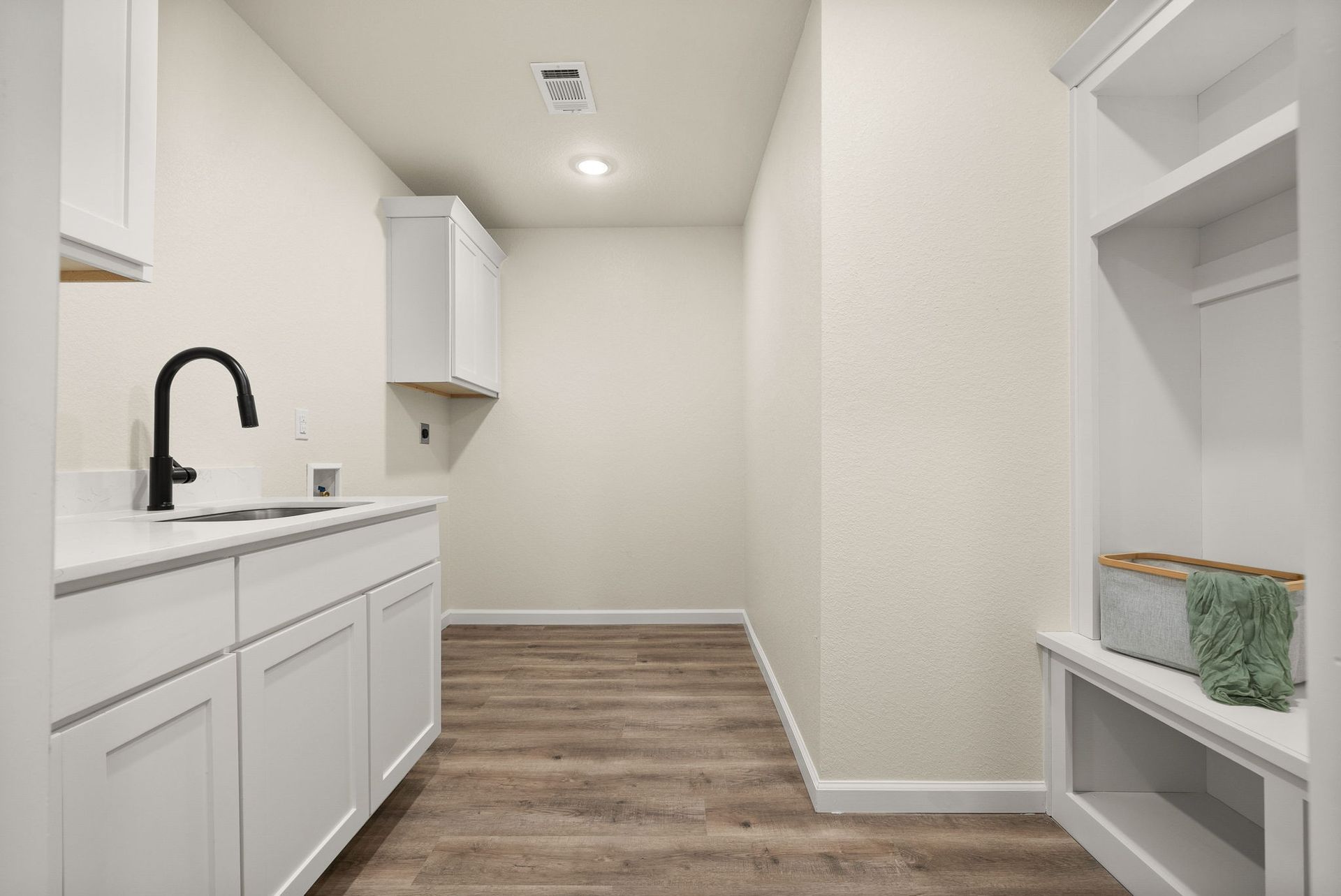 A laundry room with white cabinets , a sink , and wooden floors.