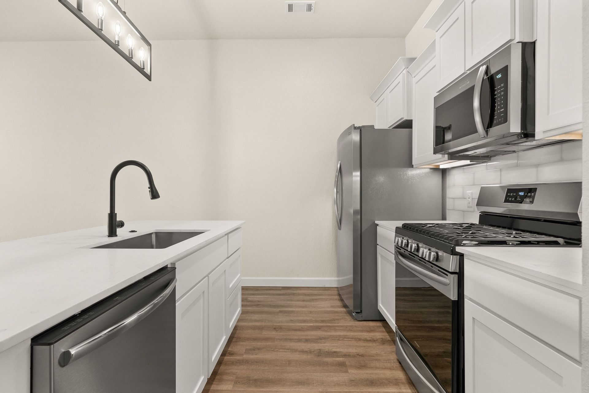 A kitchen with white cabinets , stainless steel appliances , a sink , and a refrigerator.