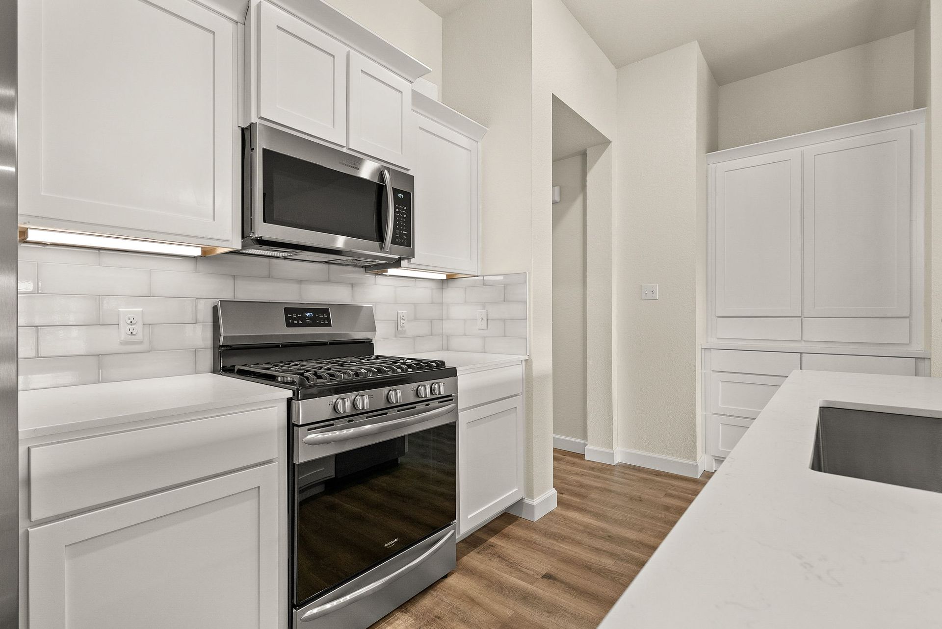 A kitchen with white cabinets , a stove , microwave , and sink.