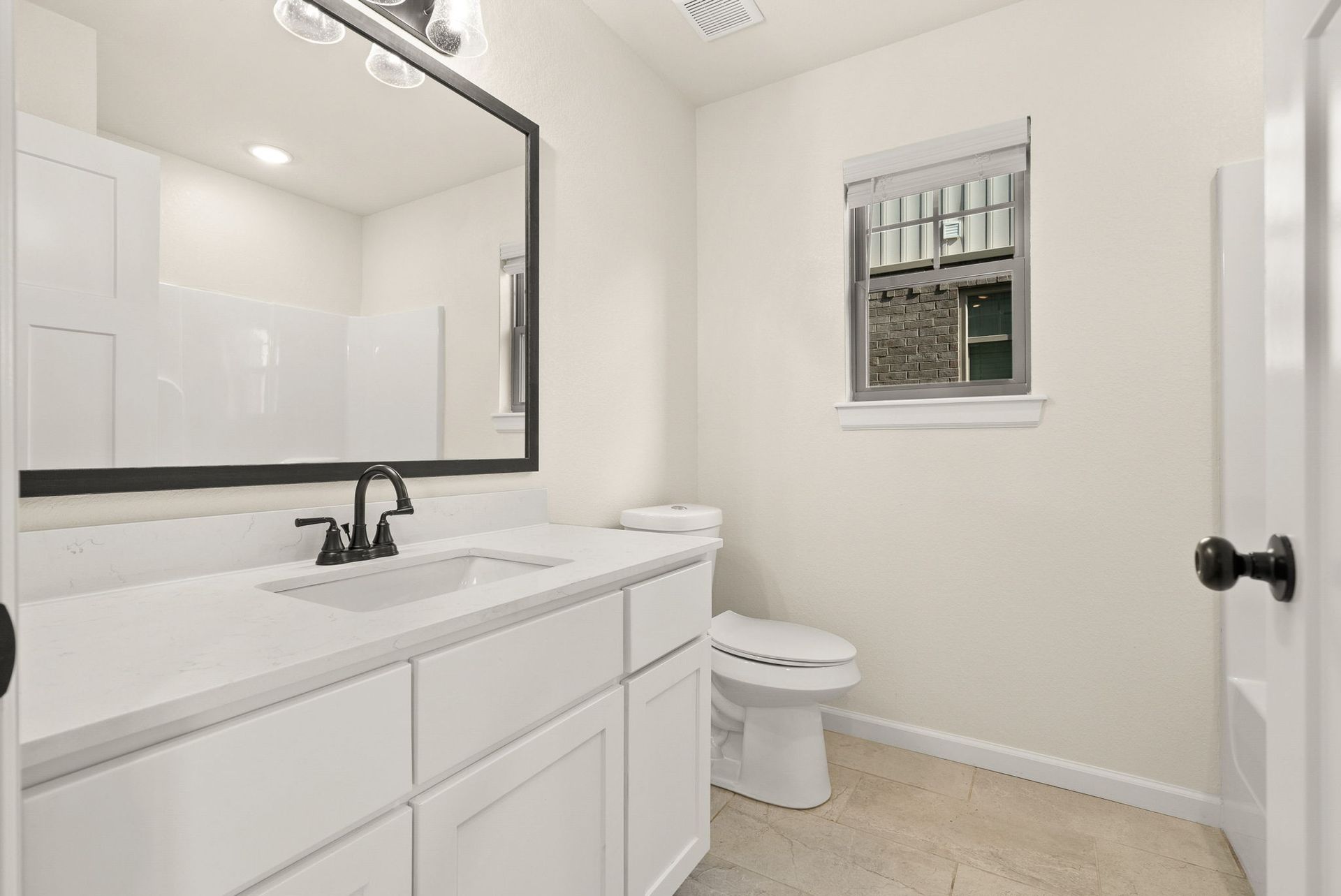 A bathroom with a sink , toilet , mirror and window.